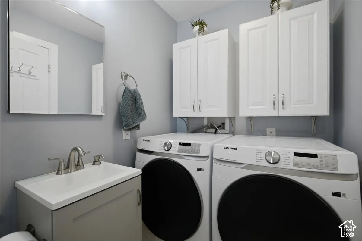 Laundry area with white upper cabinetry, a single basin vanity with a brushed nickel faucet, and front-loading laundry machines
