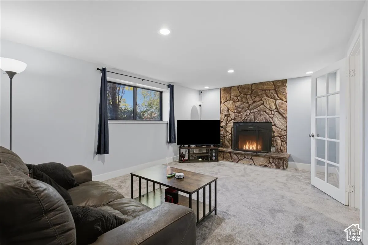Corner stone-clad fireplace, recessed lighting, window with exterior exposure, and light-toned carpeting
