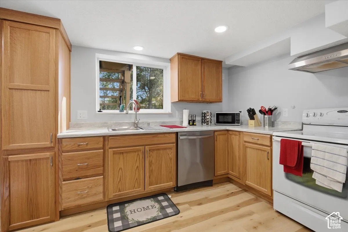 Kitchen featuring wood-finish cabinetry, light-toned countertops, a stainless steel dishwasher, a white electric range, and wood-finish flooring