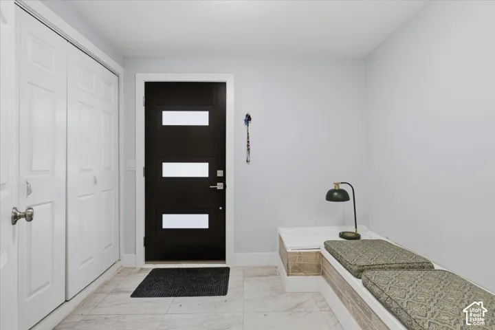 Entryway featuring a dark wood-finish door with frosted glass inserts, light tile flooring, and white bi-fold closet doors