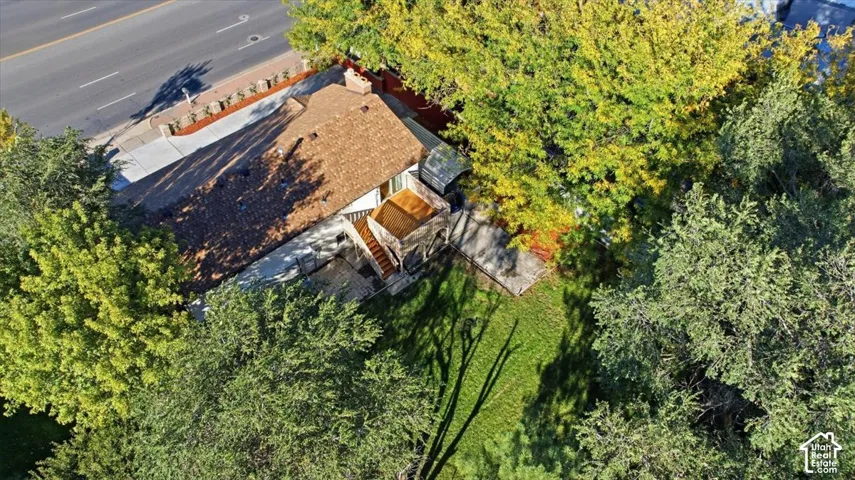 Brown shingle roof with a chimney, surrounding lush green and yellow foliage, and a landscaped front yard with a concrete driveway