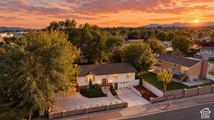 Two-car garage, concrete driveway, front entrance with double doors, established trees, and surrounding mountain scenery
