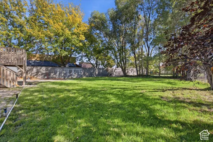 Expansive green lawn surrounded by mature trees, featuring a concrete block privacy wall and a wooden outdoor structure