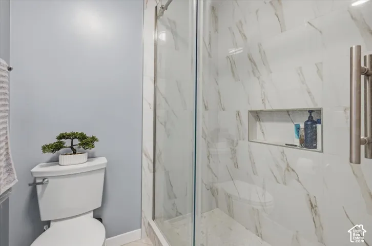 Glass-enclosed shower with a recessed niche, featuring white and gold-toned wall tiling and a mosaic tile floor