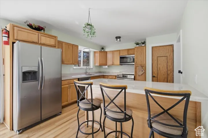 Kitchen featuring wood-finish cabinetry, stainless steel appliances, a breakfast bar, and light-toned countertops