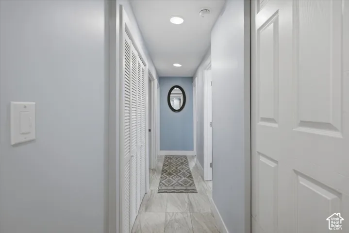 Recessed lighting illuminates the hallway, featuring wood-finish tile flooring and shutter-style closet doors