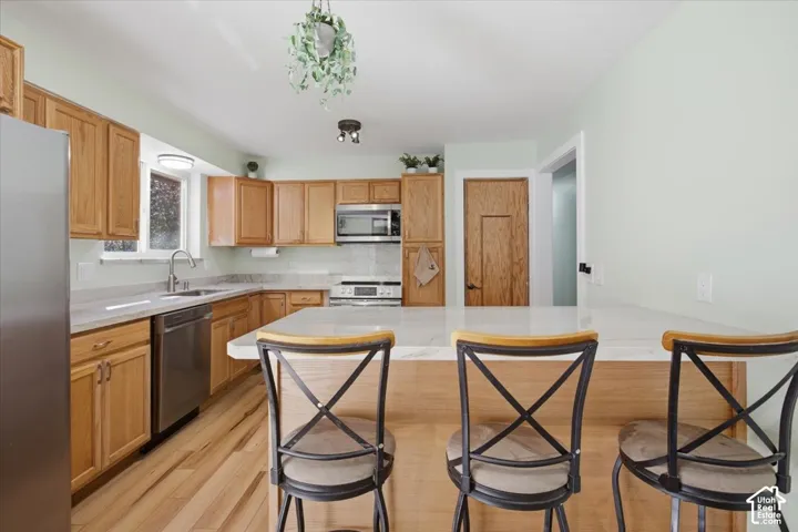 Kitchen featuring wood-finish cabinetry, stainless steel appliances, a white countertop, light wood-finish flooring, and a kitchen island with seating
