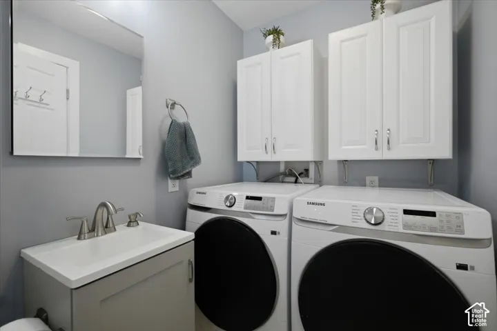 Laundry area with white upper cabinetry, a single basin vanity with a brushed nickel faucet, and front-loading laundry machines