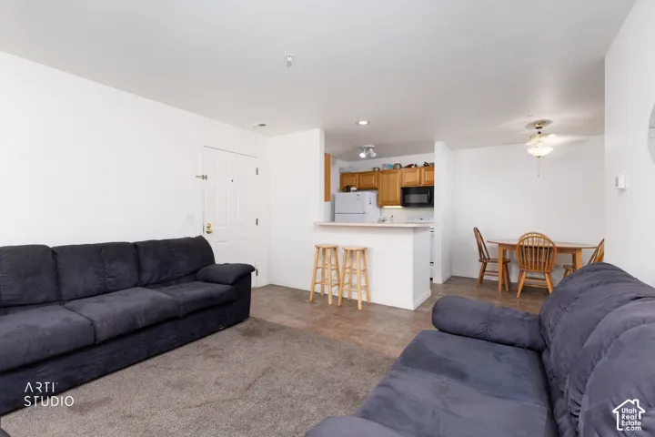 Open-concept living area with carpet flooring, a breakfast bar, wood-finish cabinetry, and a ceiling fan