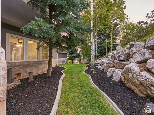 Manicured lawn with concrete edging, rock retaining wall, mature trees, and landscaping mulch