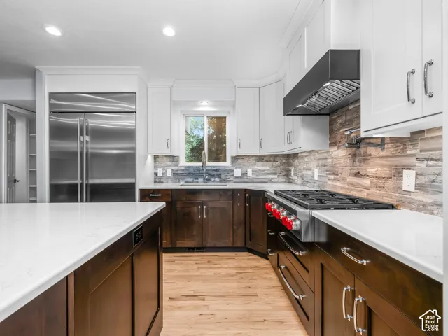 Stainless steel refrigerator and range with a pot filler, white countertops, two-tone cabinetry, and wood-finish flooring