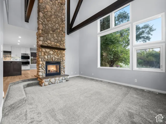 Vaulted ceiling with exposed wood beams, floor-to-ceiling stone fireplace, large picture windows, and light gray wall paint