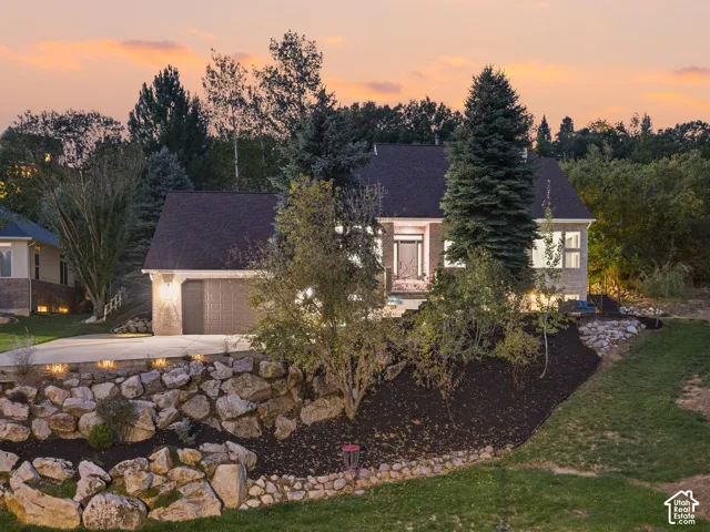 Brick facade home featuring an attached garage, paved driveway, landscape lighting, and rock retaining walls