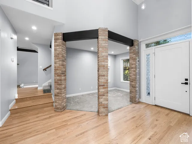 Hardwood flooring, exposed brick pillars, and a white entry door with decorative glass panels