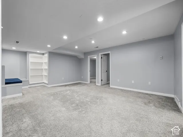 Recessed lighting illuminates a spacious room featuring light gray carpeting and soft gray walls