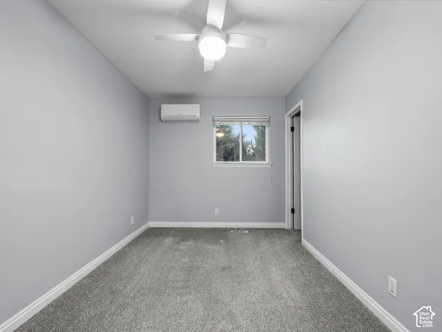 Gray carpeting, white ceiling fan, wall-mounted air conditioning unit, and a window with blinds