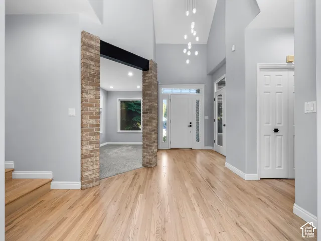 Vaulted ceilings, wood-finish flooring, brick archway, recessed lighting, and a modern chandelier