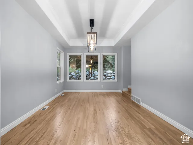 Hardwood flooring, tray ceiling with recessed lighting, modern chandelier, multiple windows, and white trim