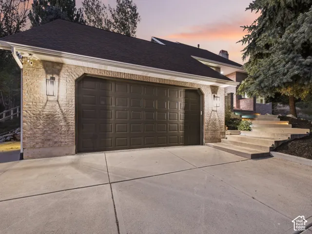 Attached two-car garage with panel doors, stone veneer facade, and exterior sconce lighting