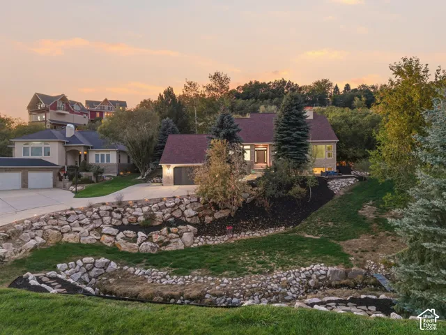 Stone retaining walls, sloped landscaping, mature trees, and a concrete driveway