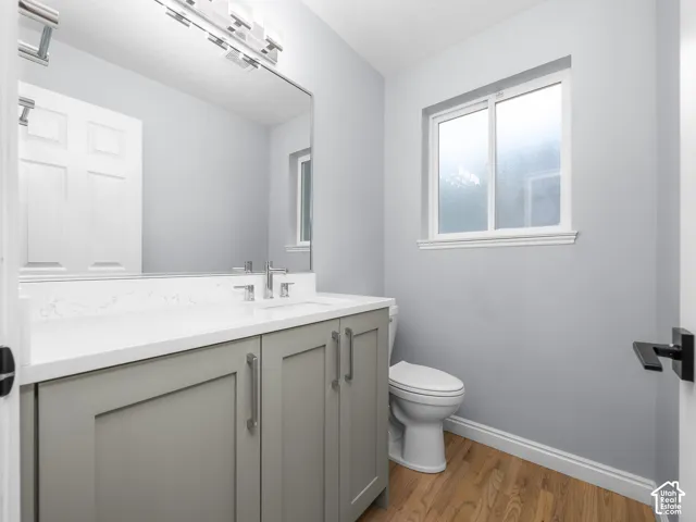 Gray vanity with a white countertop and integrated sink, chrome faucet, and wood-finish flooring