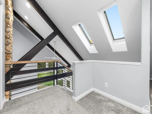 Vaulted ceiling featuring exposed beams, stone-clad pillar, and dual skylights