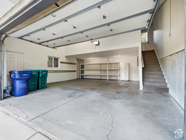 Spacious garage with concrete flooring, built-in shelving, and interior access stairs
