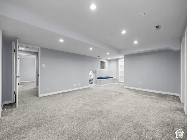 Expansive carpeted area with recessed lighting, built-in window bench, and an integrated shelving unit