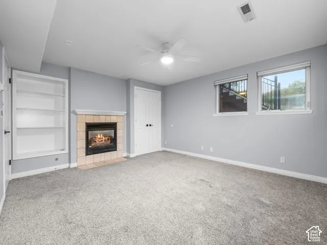 Built-in shelving, stone tile fireplace surround, light gray wall color, flush-mount lighting, and carpeted flooring