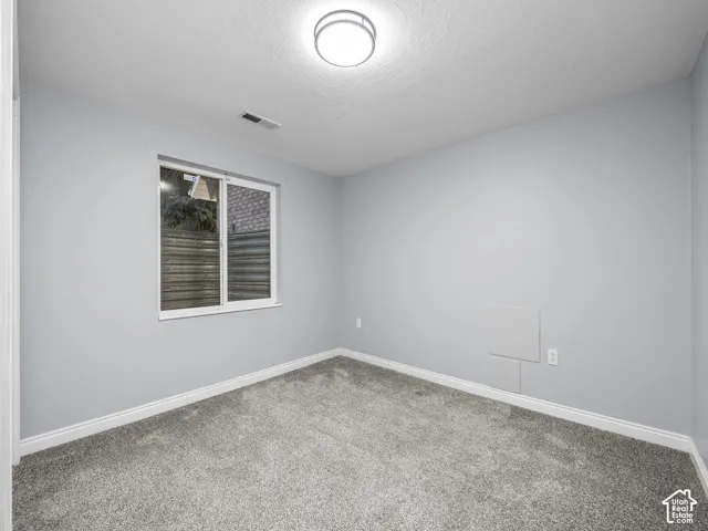 Gray carpeting, light gray wall paint, window with white trim, and a flush mount ceiling light fixture