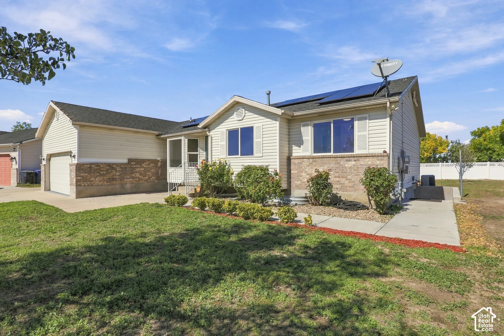 Exterior featuring light-toned siding, brick detailing, a dark-toned roof, solar panels, and an attached garage