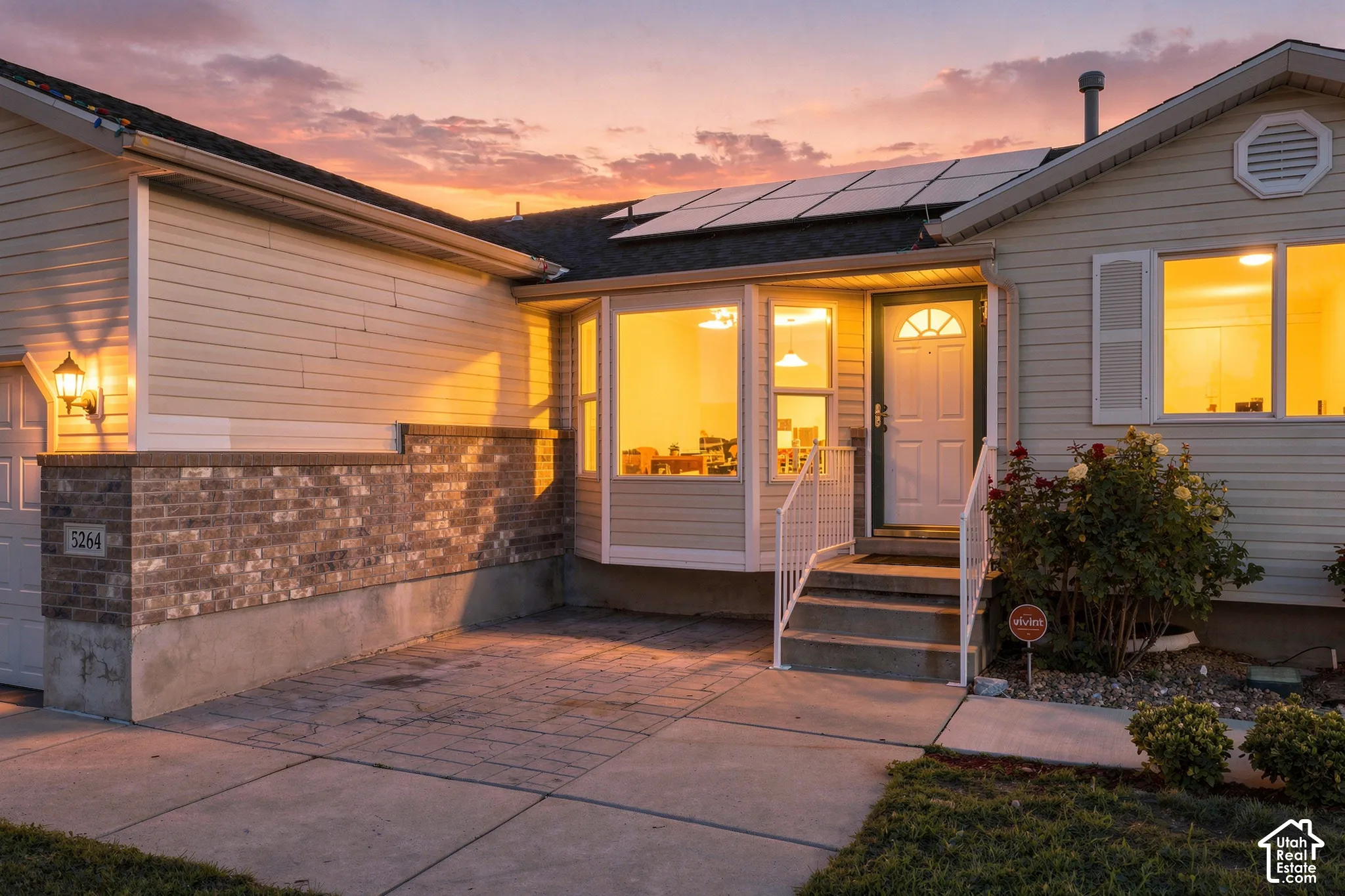 Solar panels, light-toned siding, brick exterior accent, bay window, and a front entry with handrails