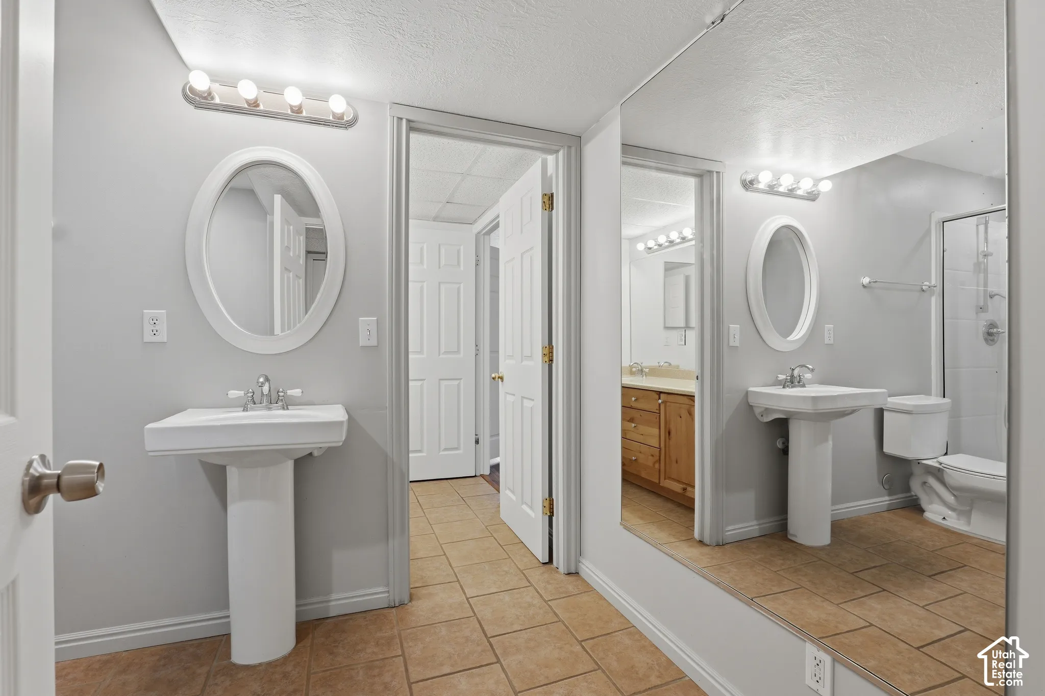 Dual pedestal sinks with oval mirrors and vanity lighting