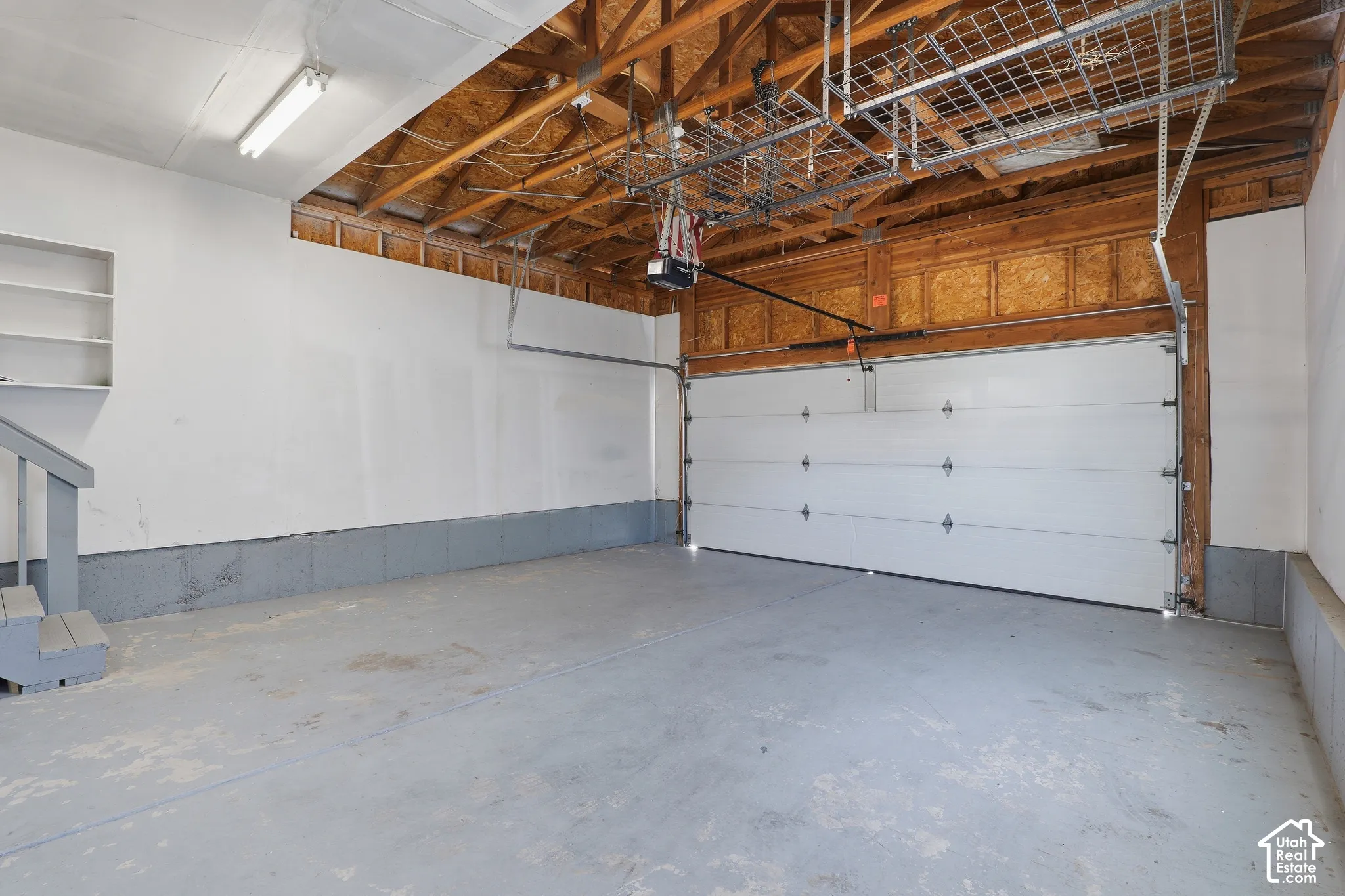 Attached garage with exposed wood rafters, concrete flooring, built-in shelving, and overhead metal storage racks