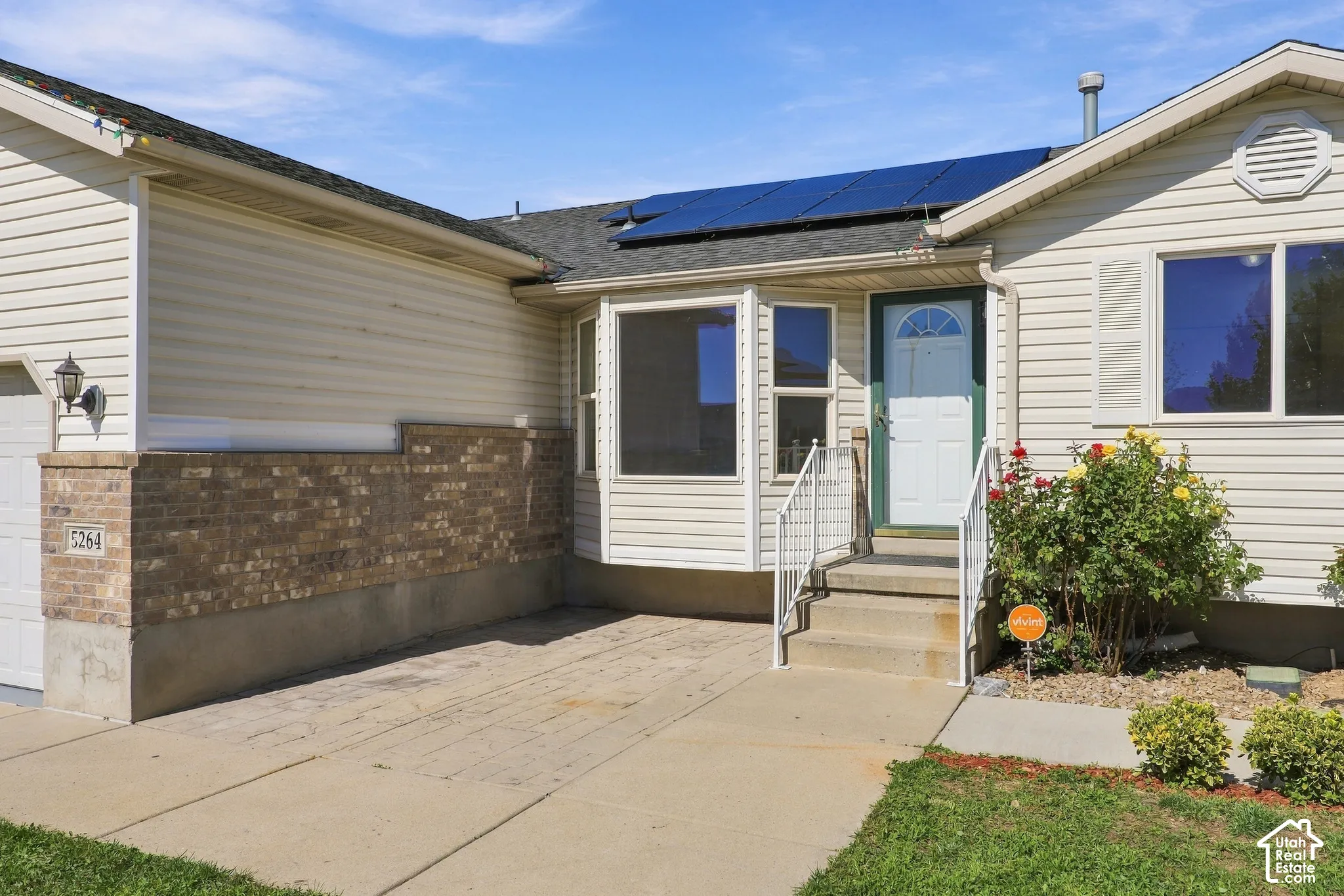 Solar panel array, neutral-toned siding, brick wainscoting, integrated garage, and a welcoming entry porch