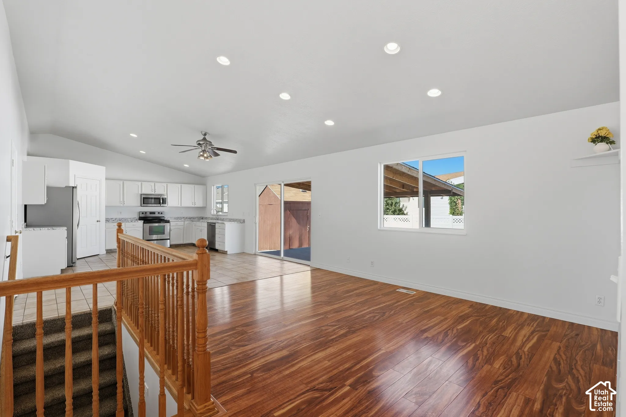 Vaulted ceilings with recessed lighting, wood-finish flooring, sliding glass patio door, white cabinetry, and stainless steel appliances