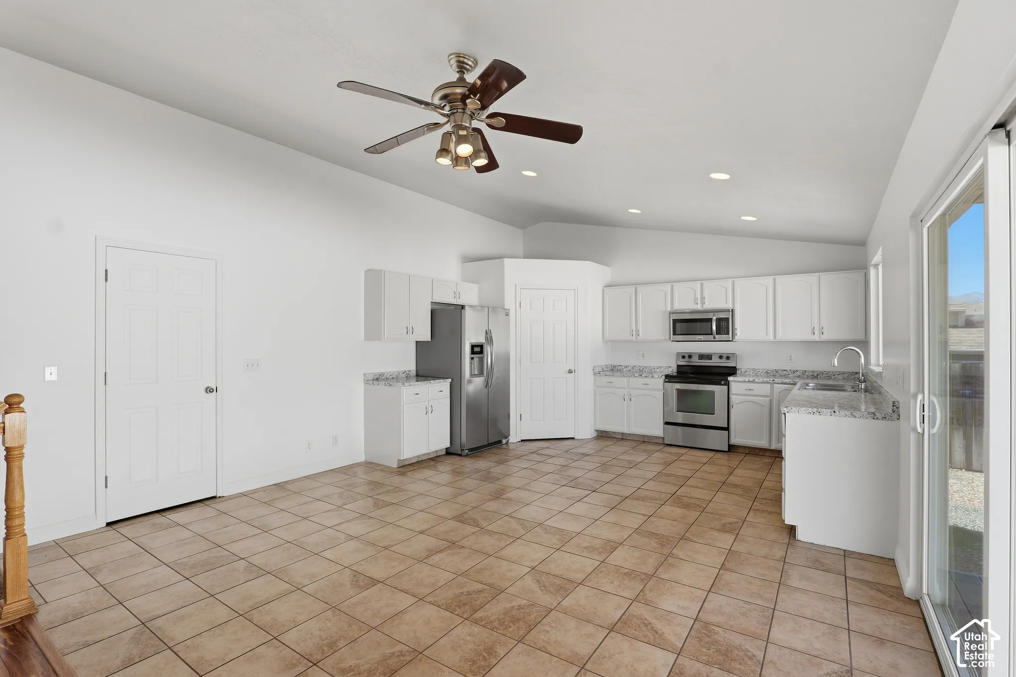 Open-concept kitchen and living area featuring tile flooring, white cabinetry, stainless steel appliances, and a ceiling fan with integrated lighting