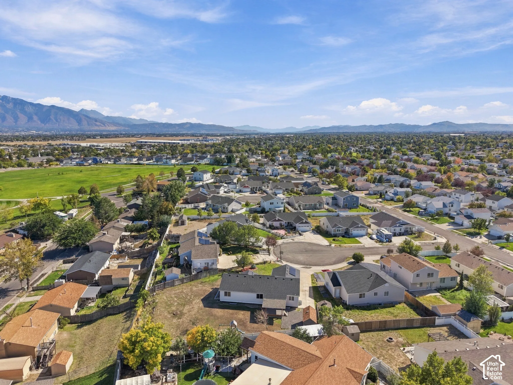 Expansive residential area featuring a green public park, surrounding mountain ranges, and numerous detached homes with varied architectural styles