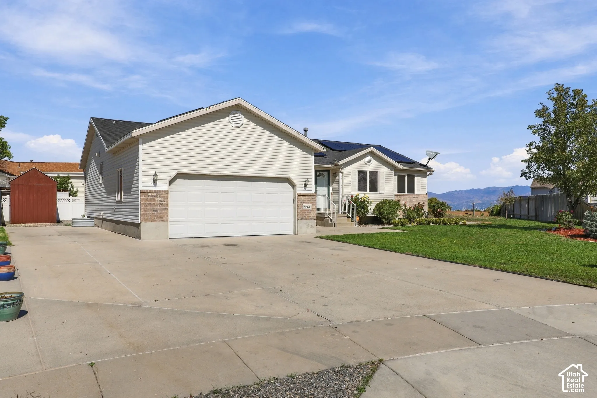 Light-colored siding exterior with brick accents, attached garage, concrete driveway, and a manicured lawn