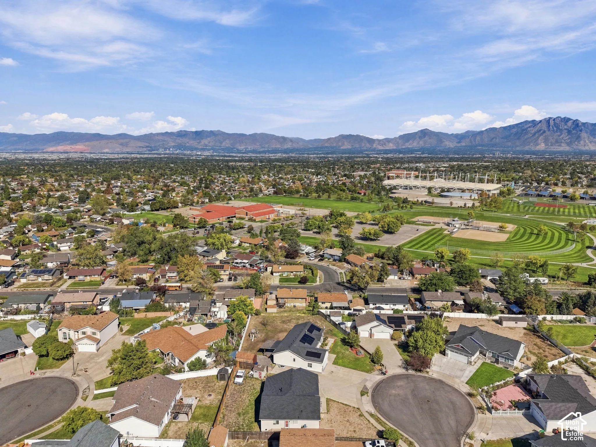 Mountain backdrop, extensive residential area, athletic fields, large institutional building, visible solar panels on rooftops