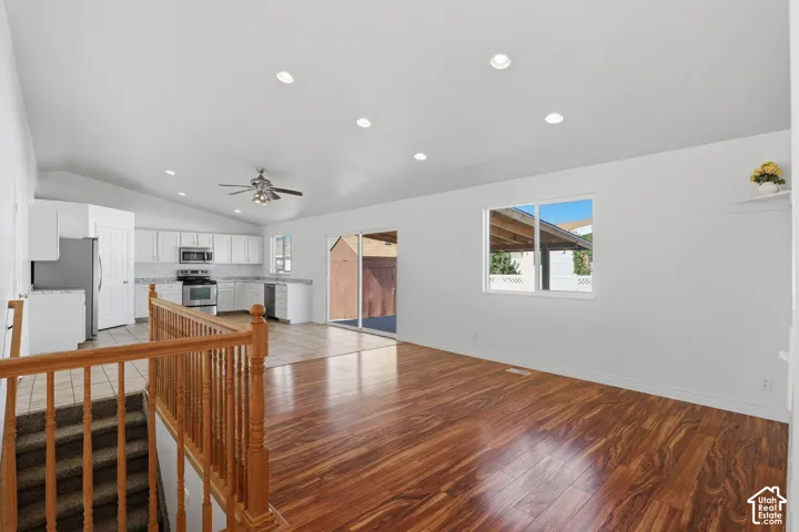 Vaulted ceilings with recessed lighting, wood-finish flooring, sliding glass patio door, white cabinetry, and stainless steel appliances