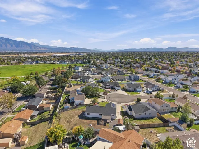 Expansive residential area featuring a green public park, surrounding mountain ranges, and numerous detached homes with varied architectural styles