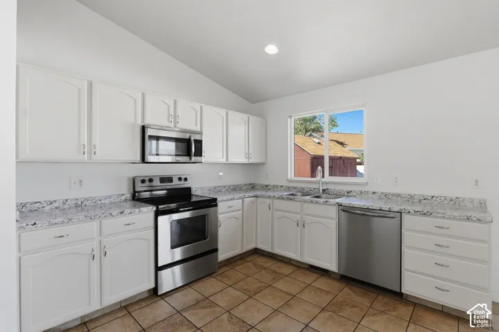Kitchen featuring white cabinetry, stainless steel appliances, speckled countertops, and tile flooring