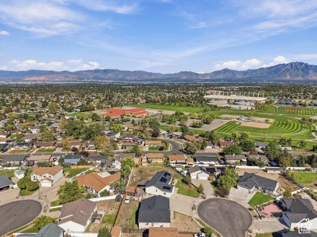 Mountain backdrop, extensive residential area, athletic fields, large institutional building, visible solar panels on rooftops