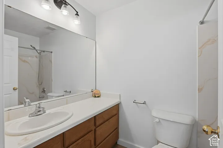 Bathroom featuring a full-width vanity mirror, a single basin sink with chrome fixtures, wood-finish cabinetry, and a shower with patterned wall panels