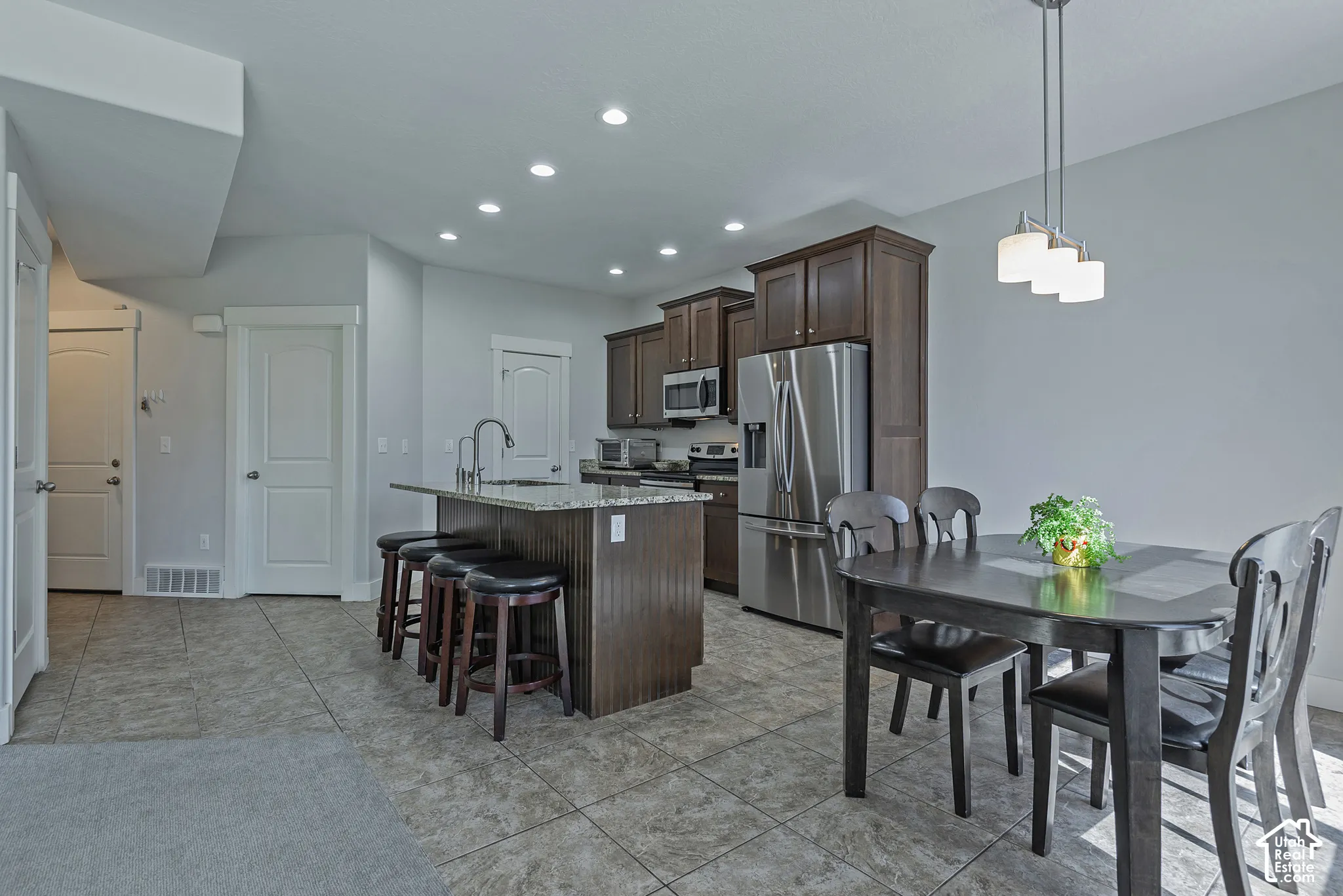 Kitchen with dark wood cabinetry, stainless steel appliances, recessed lighting, and a center island with a built-in sink