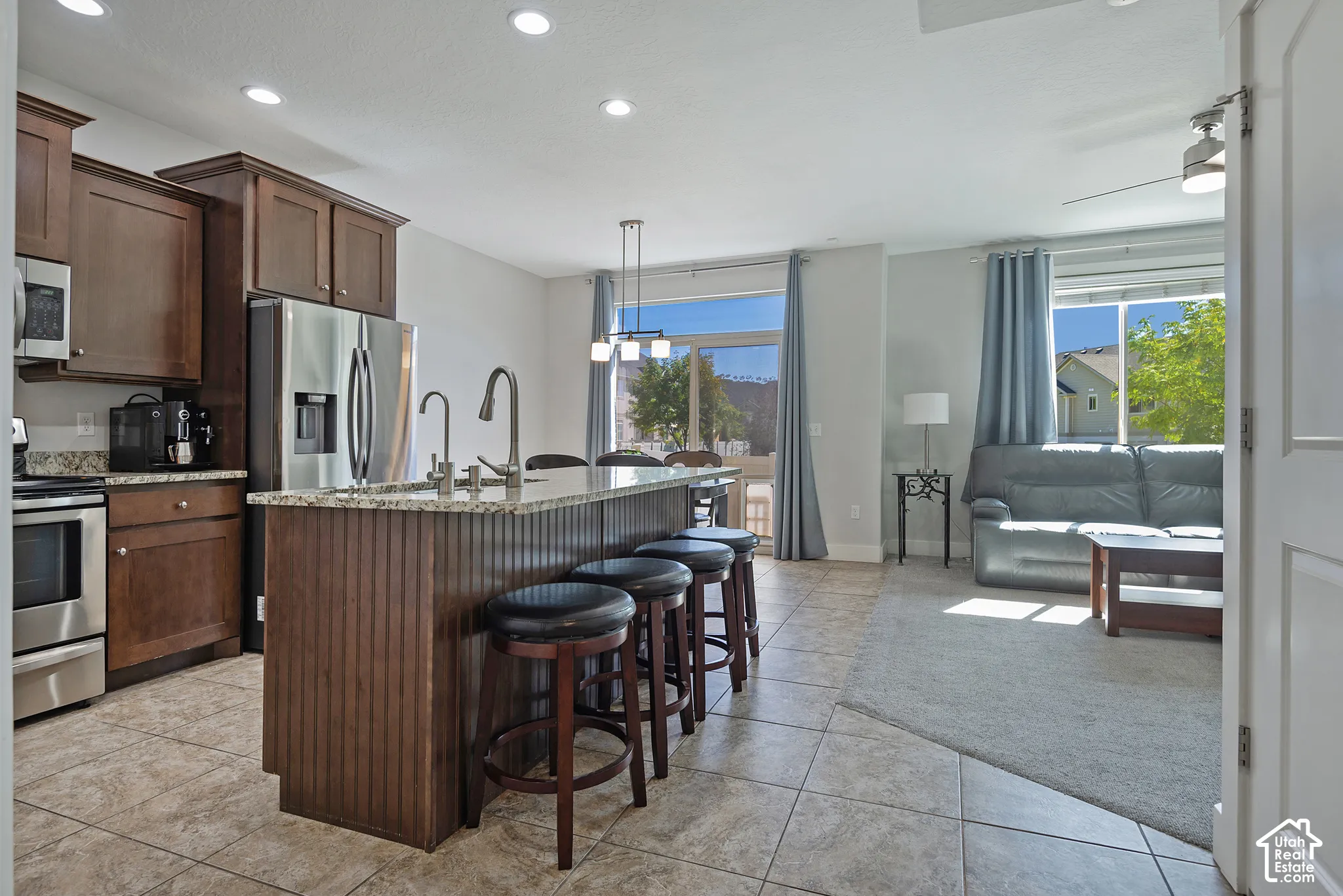Open-concept kitchen featuring dark wood cabinetry, stainless steel appliances, a center island with bar seating, and tile flooring