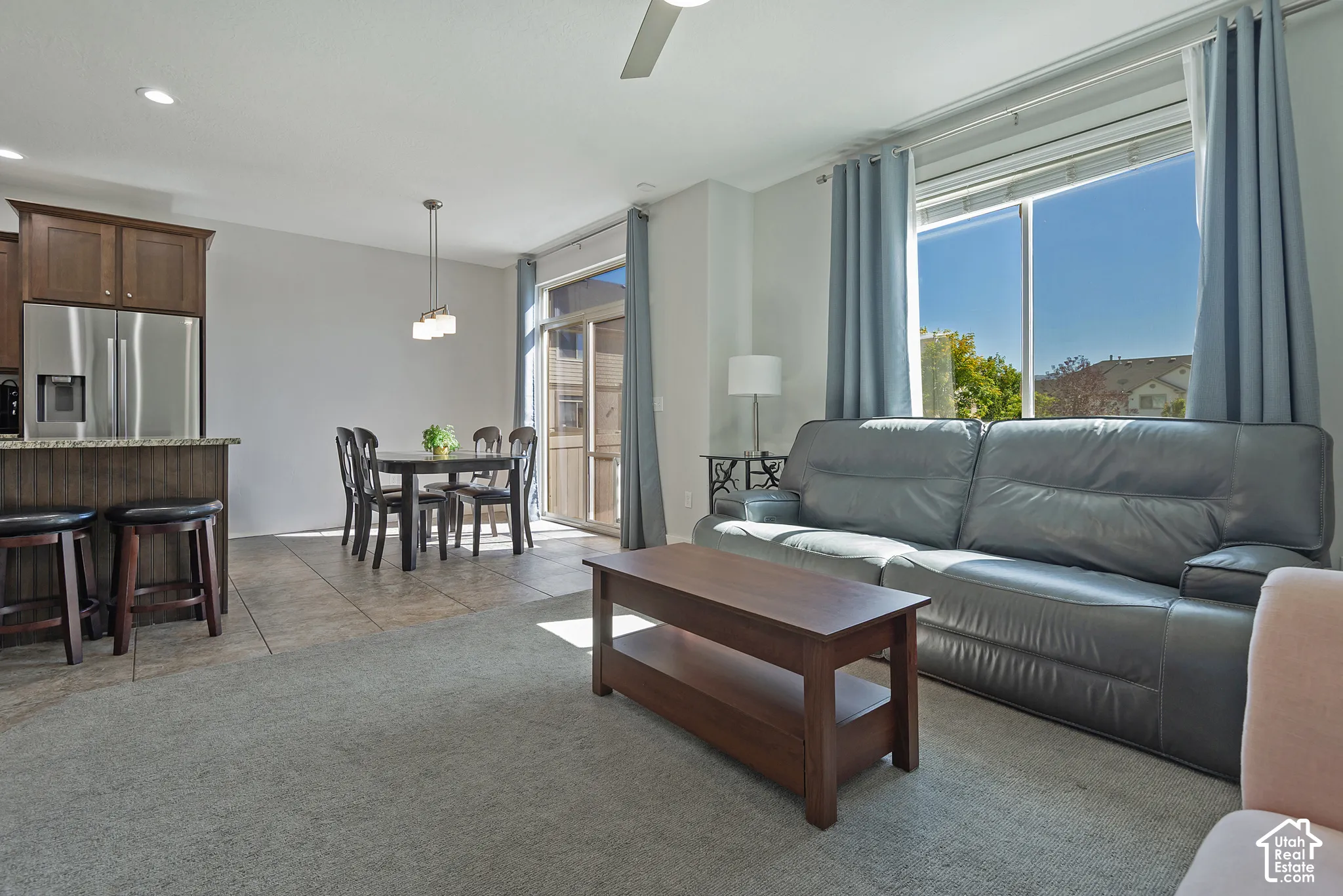 Open-concept living area with carpet and tile flooring, a kitchen island with built-in cabinetry, stainless steel appliances, and a glass sliding door