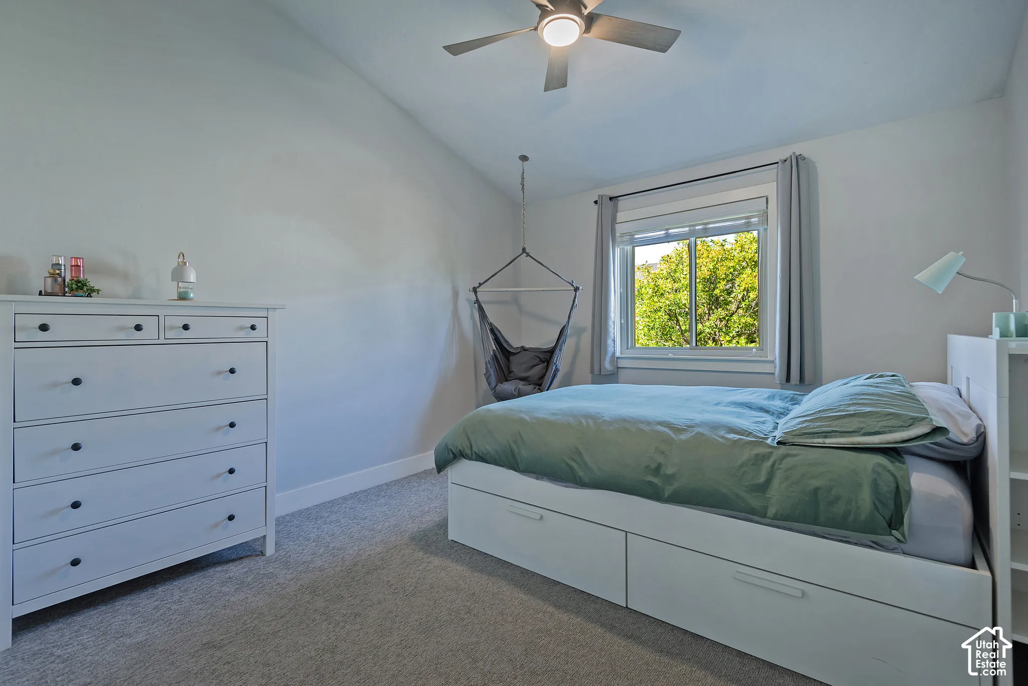 Sloped ceiling room featuring a ceiling fan with light fixture, carpeted flooring, and a window with white trim