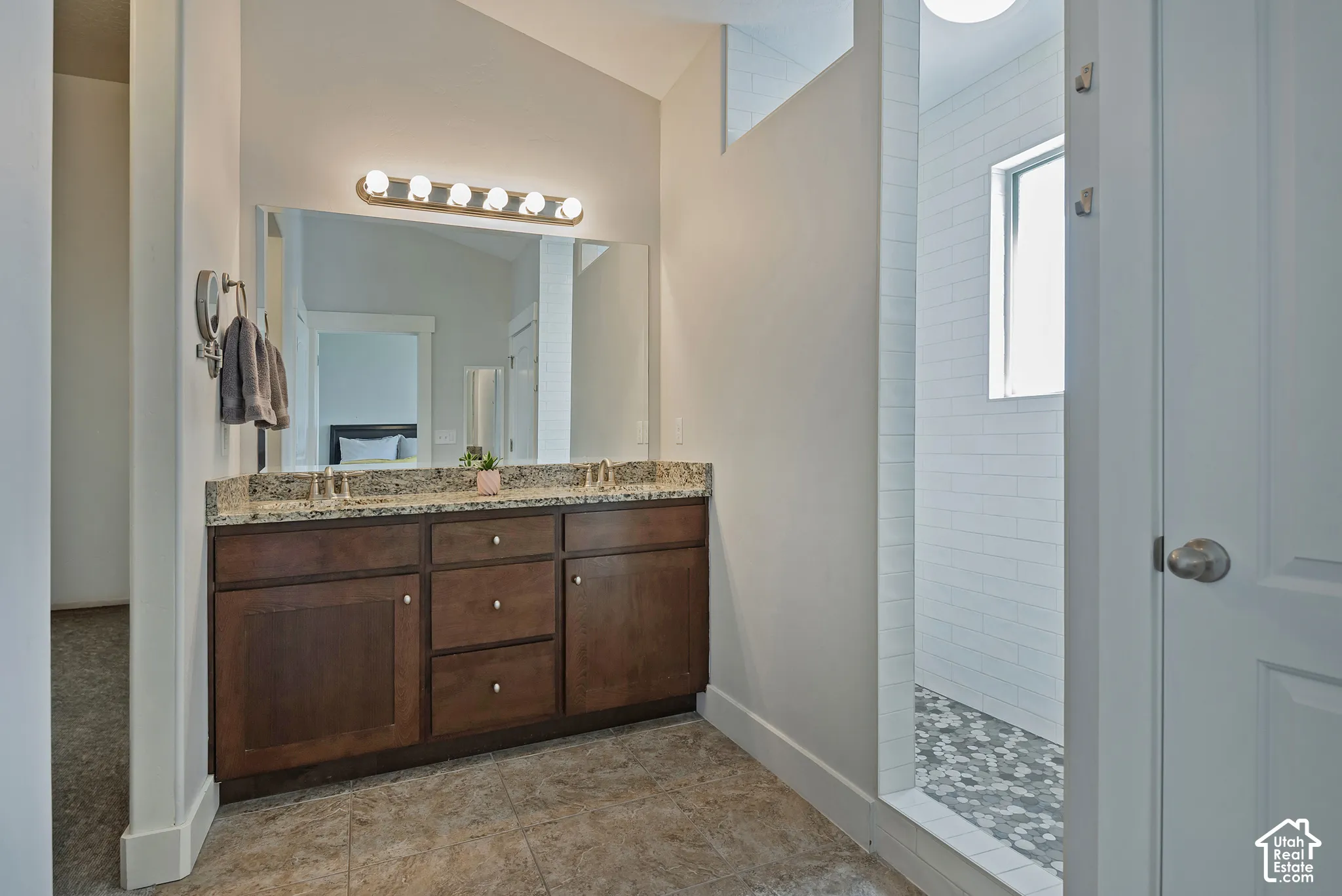 Dual sink vanity with stone countertop, wood-finish cabinetry, and tiled flooring